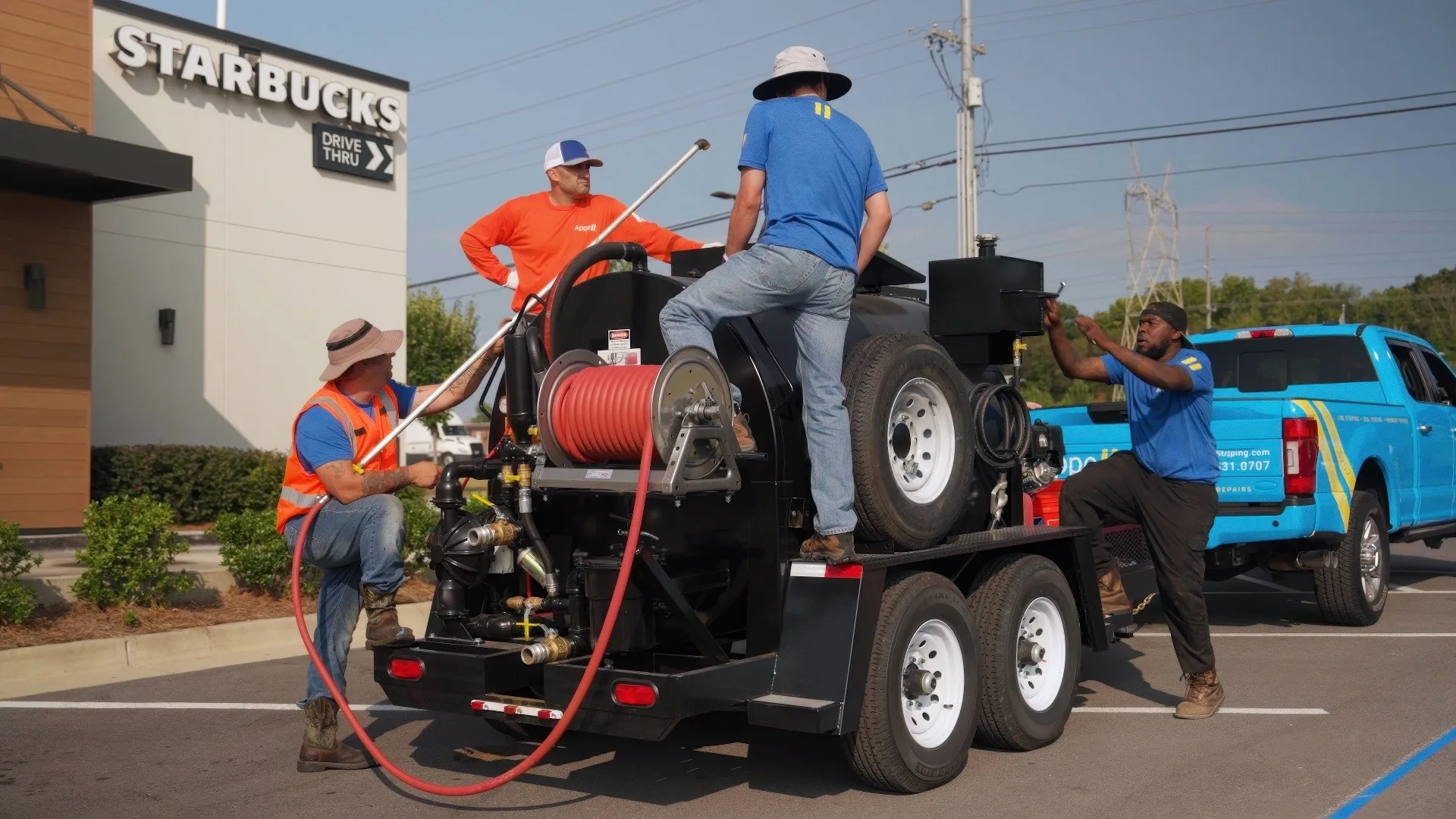 A group of workers in orange and blue uniforms operating a large cleaning machine in front of a Starbucks drive-thru.