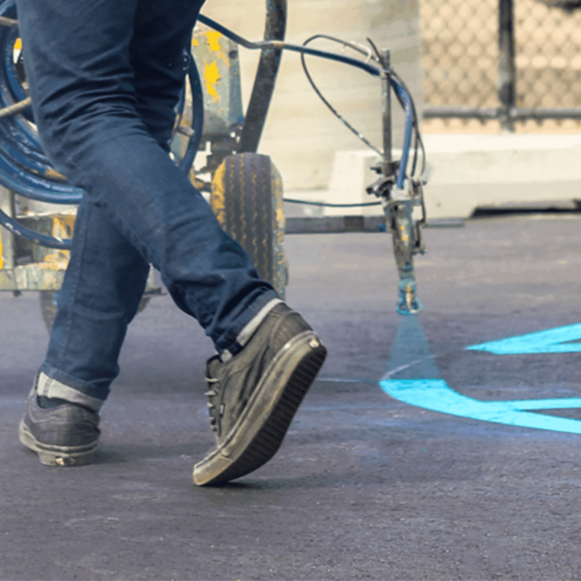 A person spray painting a blue line on the pavement, creating street art.