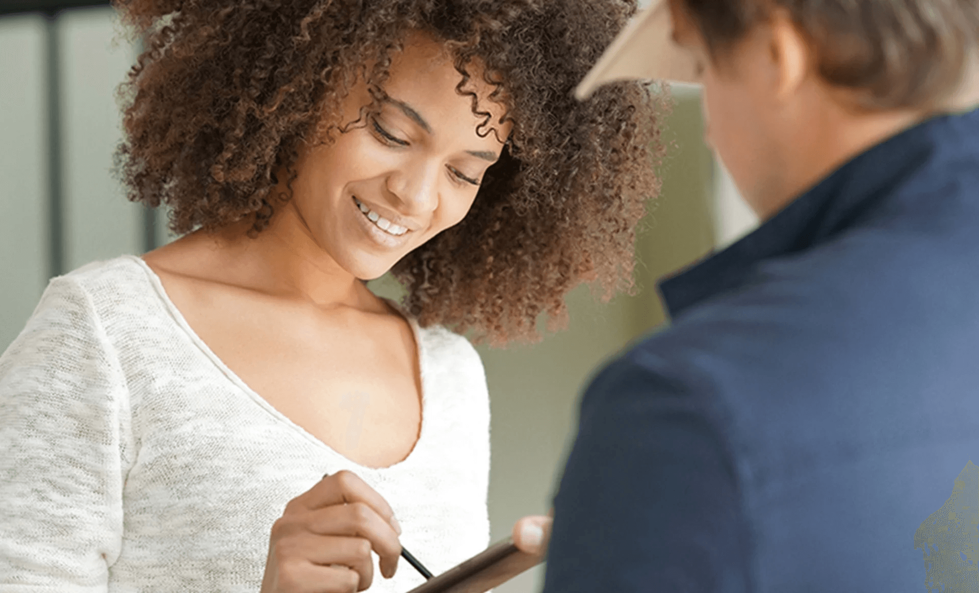 A woman smiles while using a tablet, engaging with someone off-screen.