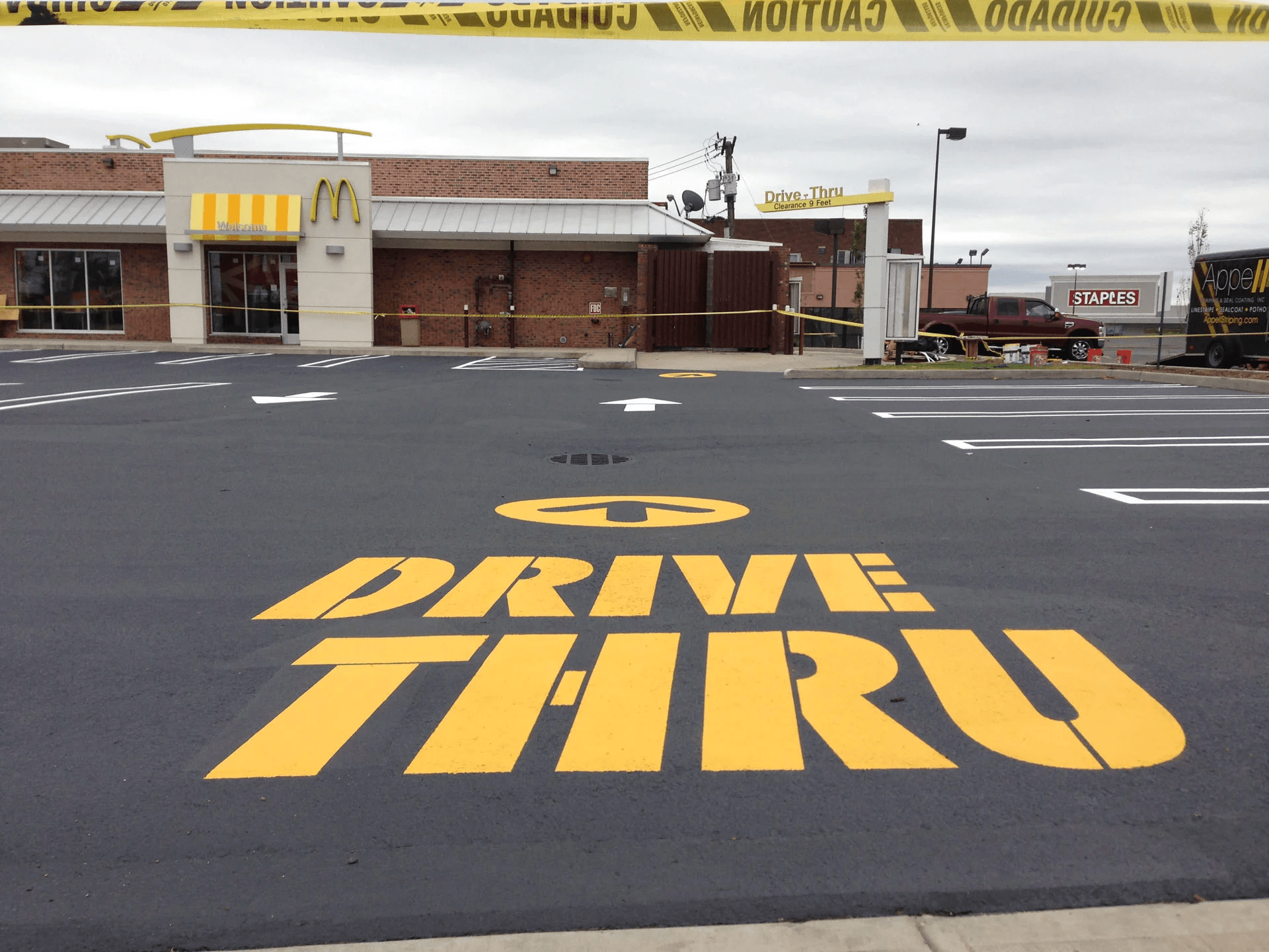 A McDonald's drive-thru area with a large 'Drive-Thru' sign painted on the asphalt, bordered by caution tape.