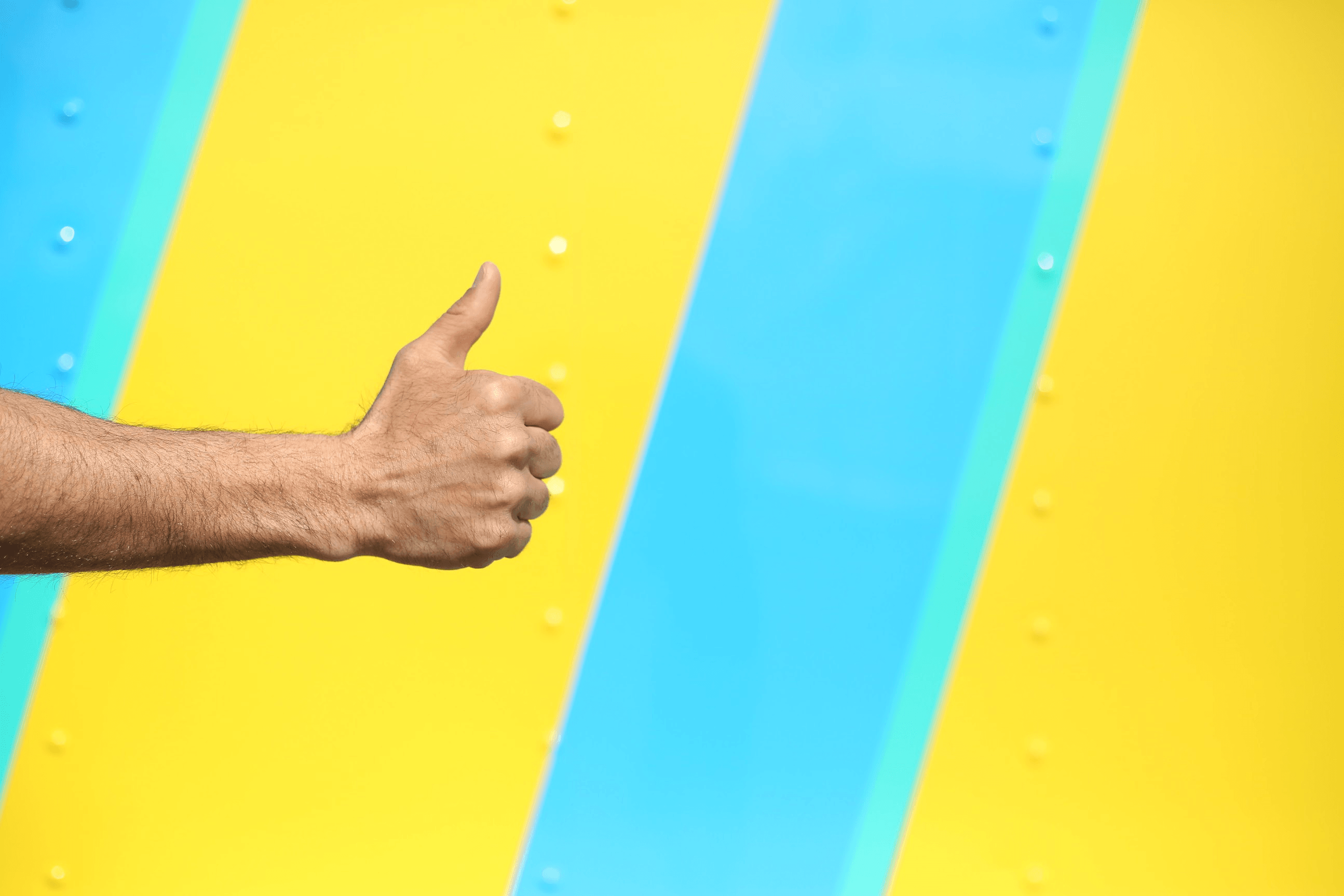 Hand giving a thumbs up against a vibrant yellow and blue striped background.