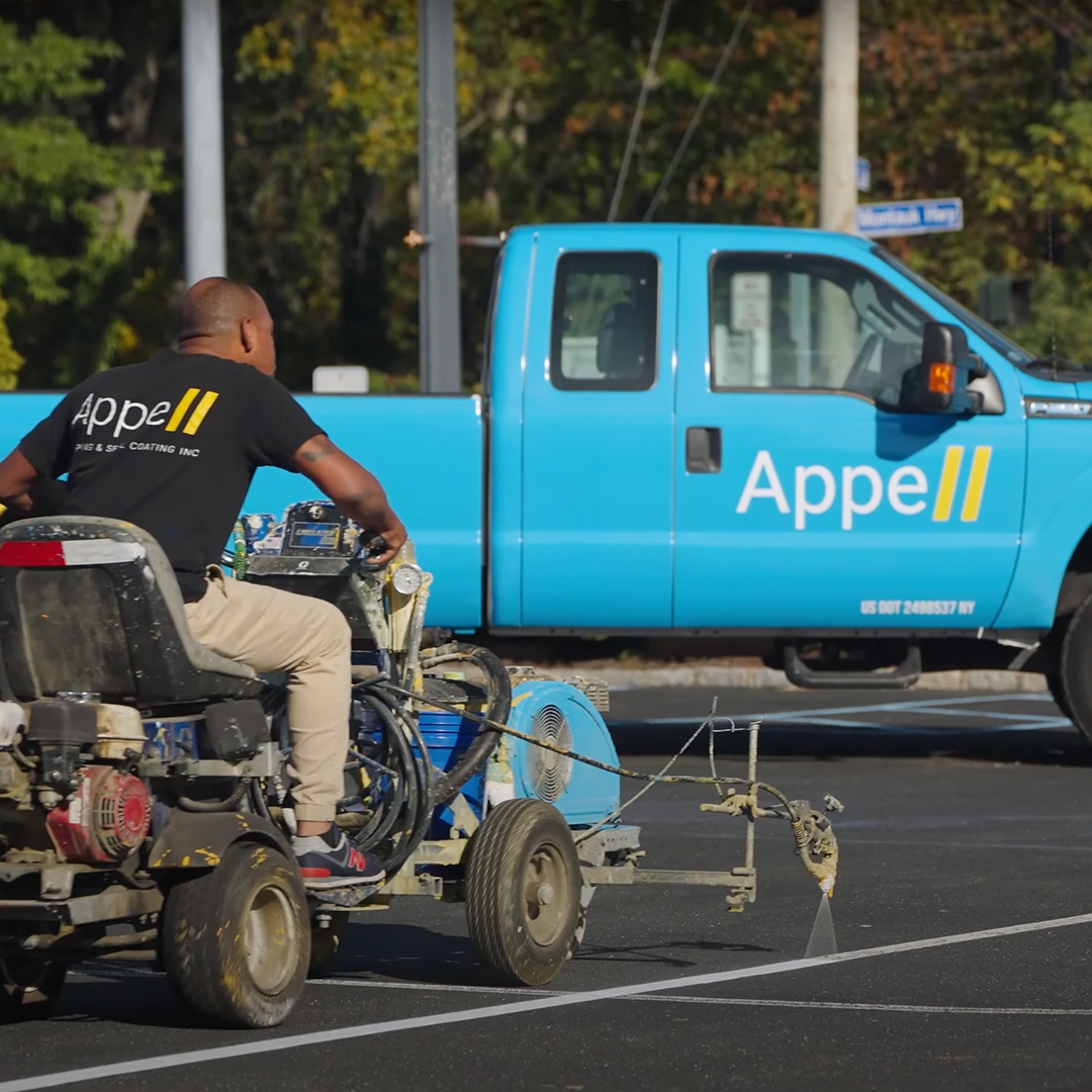 Worker using a machine to paint parking lines in a parking lot.