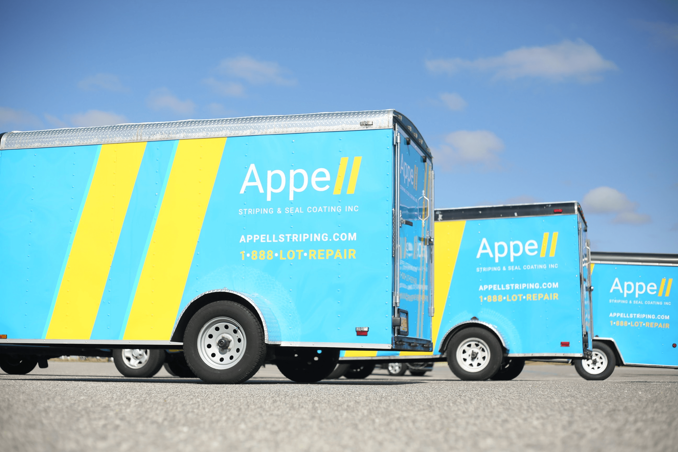 Two blue and yellow Appell Striping trailers parked under a clear sky, showcasing the company's branding and services.