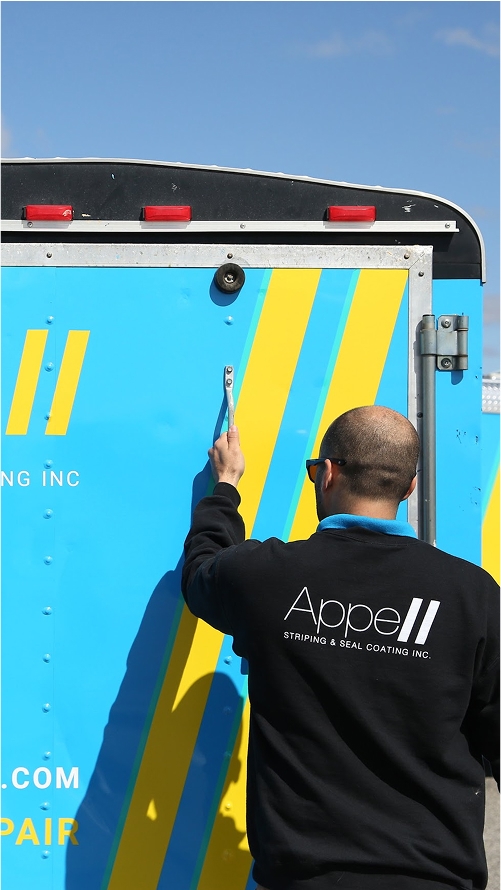 Man in black jacket with 'AppeII Stripping & Seal Coating Inc.' logo opening the door of a blue and yellow truck.